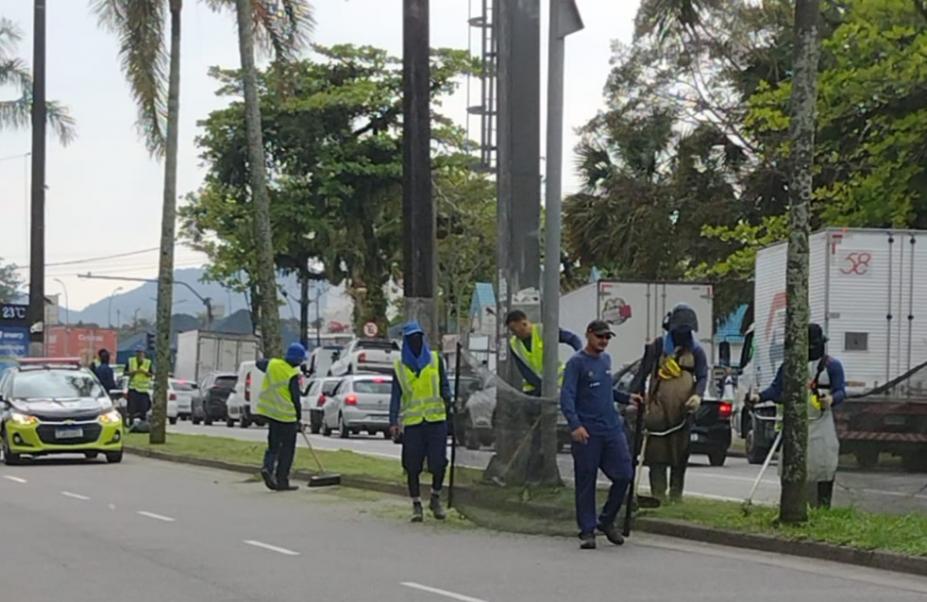homens uniformizados trabalham na manutenção de canteiro em rua. #paratodosverem