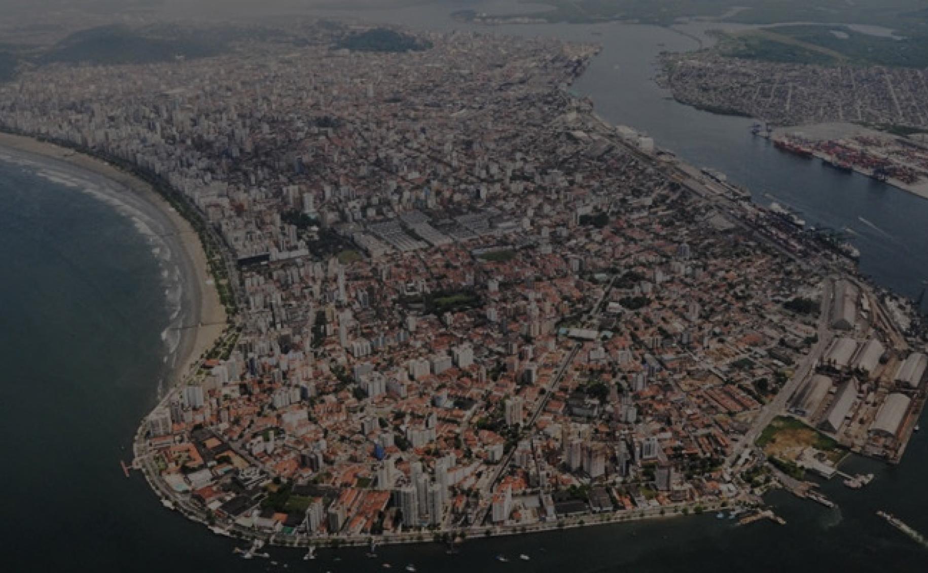 Vista panorâmica do contorno da ilha, com o porto à direita e a orla à esquerda. Há uma sobreposição cinza sobre a foto que dá um ar sombrio. #Paratodosverem