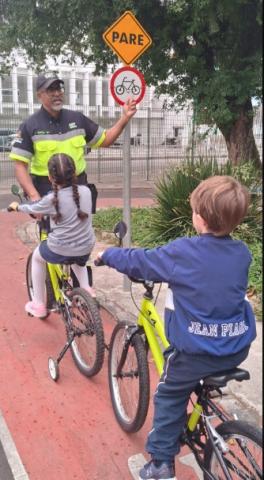 crianças de bicicleta são orientadas por agente #paratodosverem 