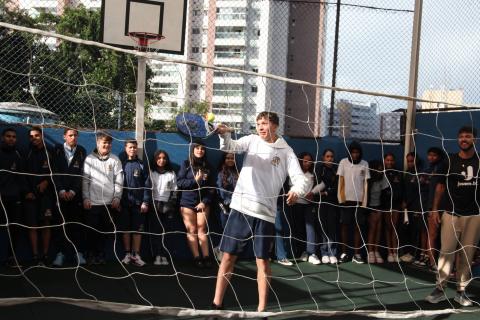aluno joga beach tennis. ele segura raquete atrás de rede. #paratodosverem