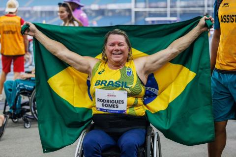 a atleta de braços aberto segurando a Bandeira do Brasil. #paratodosverem