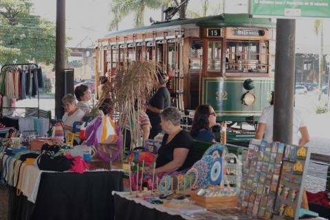 feira de artesanato com o bonde turístico ao fundo. #paratodosverem
