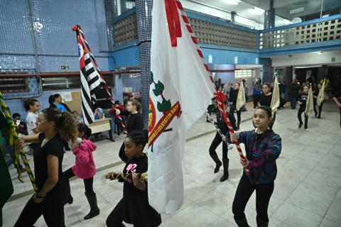 alunos carregam bandeiras e instrumentos em treinamento de banda #paratodosverem