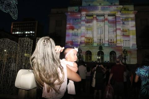 mulher com bebê assiste a projeção mapeada #paratodosverem