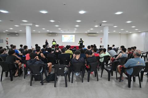 plateia sentada e duas pessoas em frente ao fundo #paratodosverem