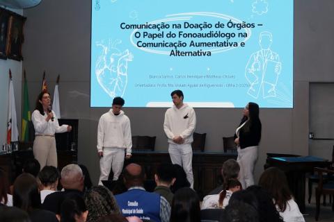 pessoas na frente de um telão olhando para a platéia #paratodosverem