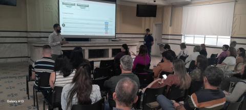 servidores reunidos em salão assistem palestra com telão. #paratodosverem