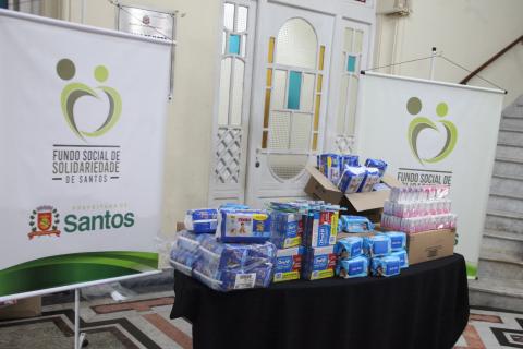 alimentos e fraldas sobre uma mesa e banner do fundo social. #paratodosverem