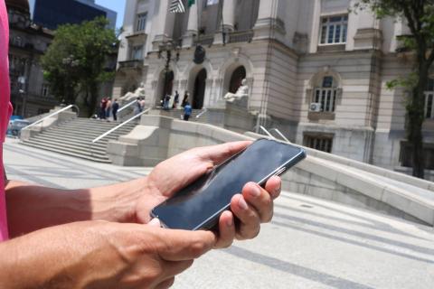 mão segura telefone celular diante da prefeitura. #paratodosverem