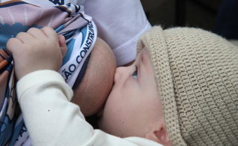 bebê olha para a mãe enquanto mama no peito #paratodosverem