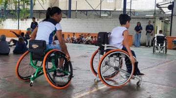 mulher e criança estão em cadeiras de rodas em quadra esportiva. #paratodosverem