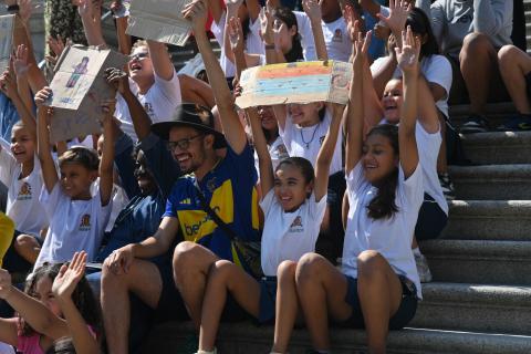 preo e criaças seguram desenhos nas mãos no alto da cabeça. #paratodosverem 