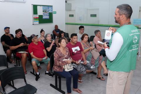 agente fala com pessoas sentadas na sala de espera #paratodosverem