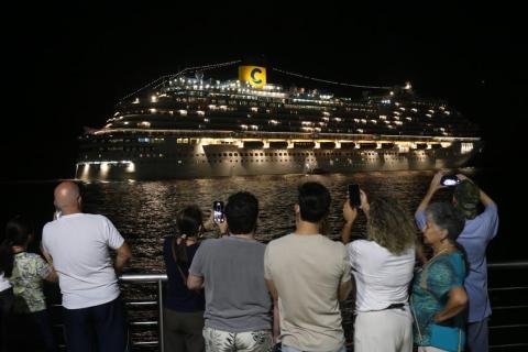 Até 4 de abril, estão previstas escalas de dez embarcações de sete companhias pessoas fotografam navio saindo à noite #paratodosverem