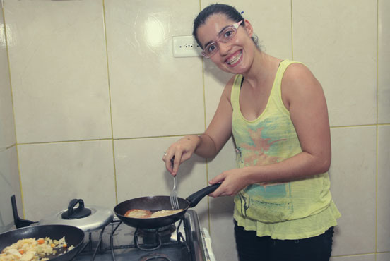 Foto de uma das usuárias do serviço cozinhando e sorrindo na unidade. #pracegover