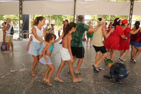 pessoas dançam sob tenda com confetes no chão. #paratodosverem