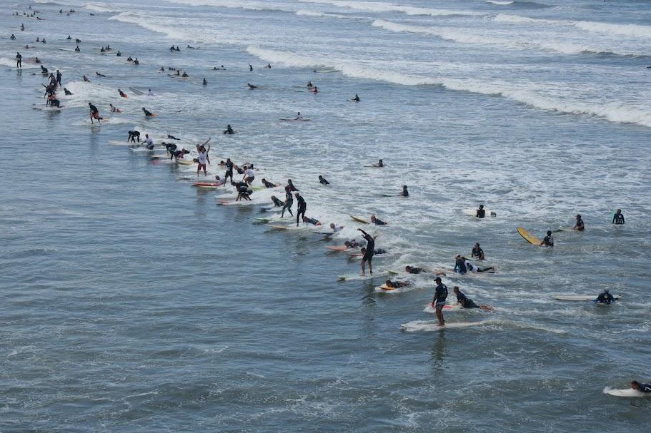 surfistas estão sobre uma mesma onda no mar em Santos. #paratodosverem